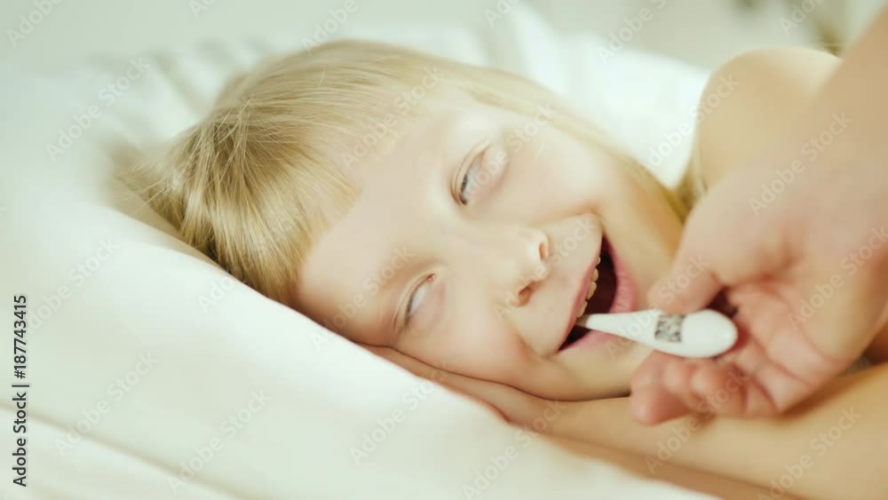 A small girl is measured by an electronic thermometer. The child lies in bed. 4k video A small girl is measured by an electronic thermometer. The child lies in bed. 4k video