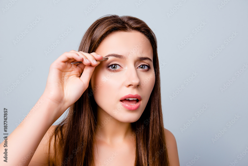 Close up photo of beautiful pretty cute charming woman using tweezers for plucking her eyebrows, isolated on grey background Close up photo of beautiful pretty cute charming woman using tweezers for plucking her eyebrows, isolated on grey background