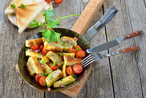 Gebratene schwäbische Maultaschen mit Speck und geschmorten Kirschtomaten im Eisenpfandl  serviert - Fried Swabian meat ravioli with bacon and roasted cherry tomatoes served in an iron frying pan photo