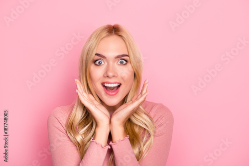 Wow, sale. Close up portrait of young pretty woman with long blond hair looking exited holding her mouth open, hands near cheeks, looking shocked, surprised, standing over pink background