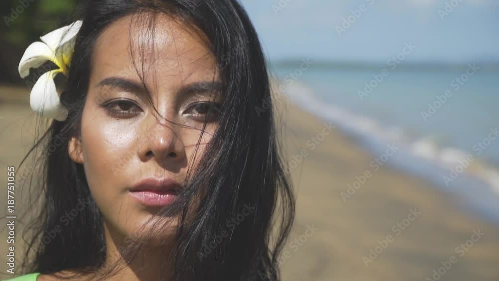 Close-up of a face of a beautiful asian girl walking along the beach with a tropical flower in her hair. Thailand. Close-up of a face of a beautiful asian girl walking along the beach with a tropical flower in her hair. Thailand.
