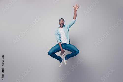 Full-size full-length portrait of cheerful handsome joyful excited delightful impressed surprised afro guy wearing casual denim jeans clothing jumping up, isolated on gray background