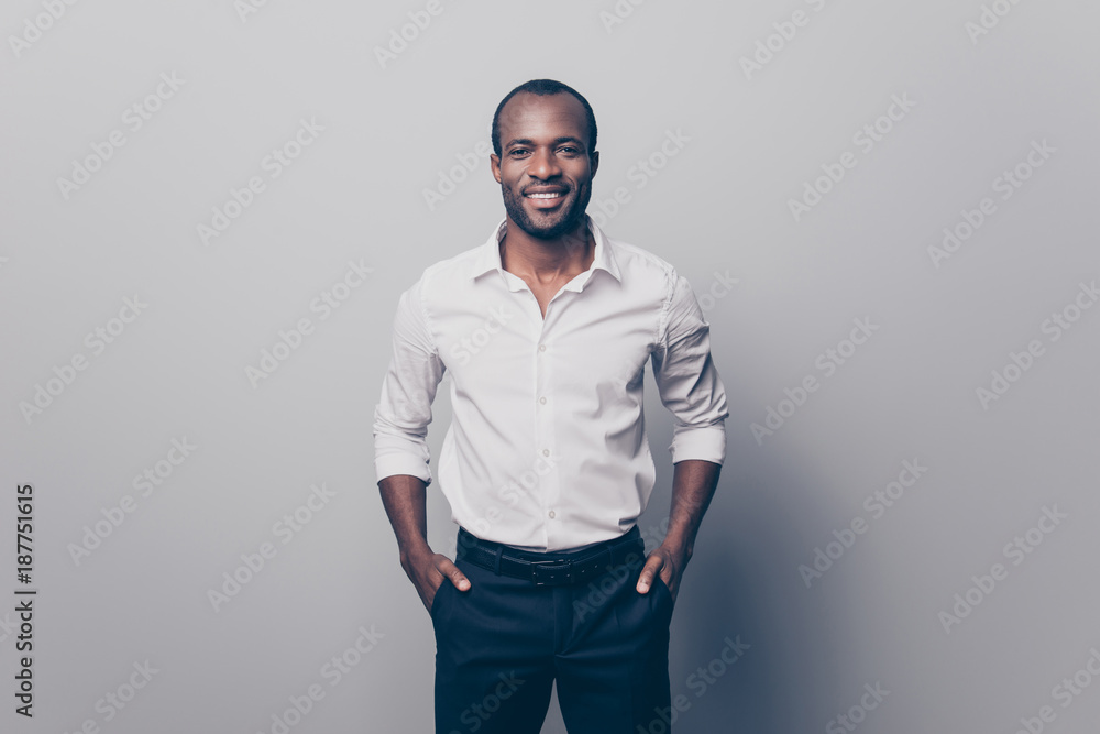 Portrait of glad confident intelligent attractive african man wearing white  shirt with rolled-up sleeves holding hands in pockets isolated on gray  background Stock Photo | Adobe Stock