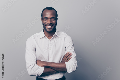Portrait of confident experienced qualified smart intelligent clever laughing afro man with toothy beaming smile dressed in white classic shirt with folded hands isolated on gray background