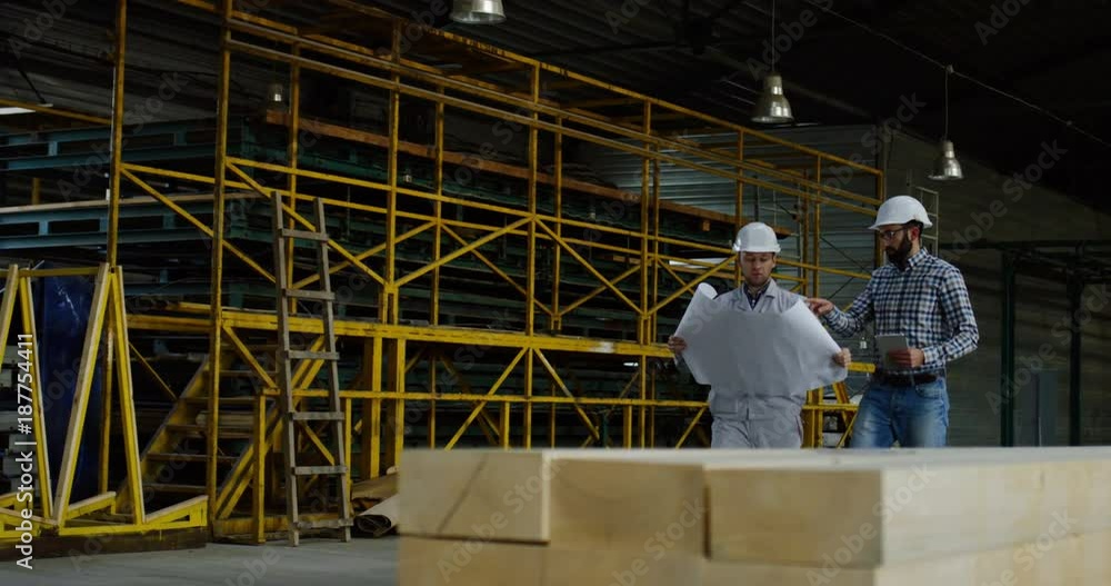 Two man talking and walking in the furniture factory with paper documents in their hands. Inside. Two man talking and walking in the furniture factory with paper documents in their hands. Inside.