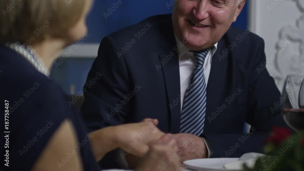 Tilt up of shy senior man with flushed cheeks holding hand of his