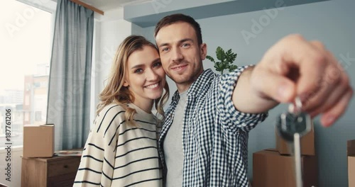 Happy couple in love showing keys of purchased apartment in new house. Young attractive people smiling and looking at camera. Indoors.