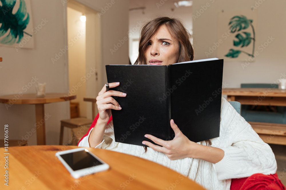 Portrait of a confused woman holding blank cover notepad Portrait of a confused woman holding blank cover notepad