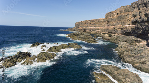 Rough sea with waves over rocks by granite cliffs  Atlantic Ocean coast  Fuerteventura  Canary Islands  Spain .