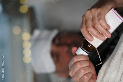 Sick man opening a cough syrup bottle. Selective focus