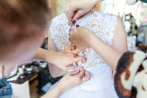 Bridesmaid helping bride with her wedding dress. Wedding day details
