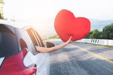 Relaxed happy traveler, Young beatiful asian gilr holding red heart and Reach out of the car at sunset and beautiful view with mountain road background