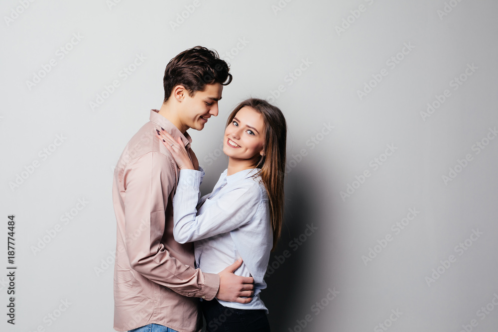 Vertical photo of two young cheerful people hugging each other against gray Vertical photo of two young cheerful people hugging each other against gray