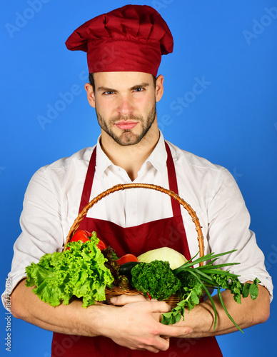 Cuadro en lienzo Cook with serious face holds wicker basket of fresh veggies.