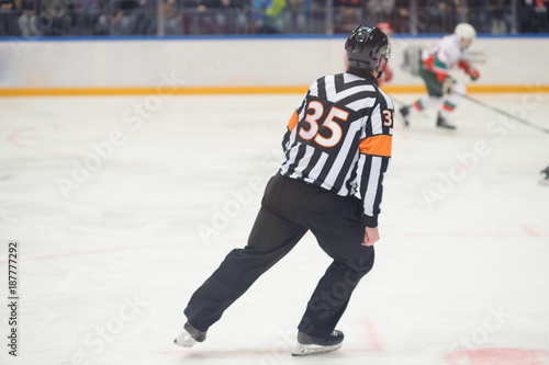 Hockey referee rides on ice on ice skates, hockey players