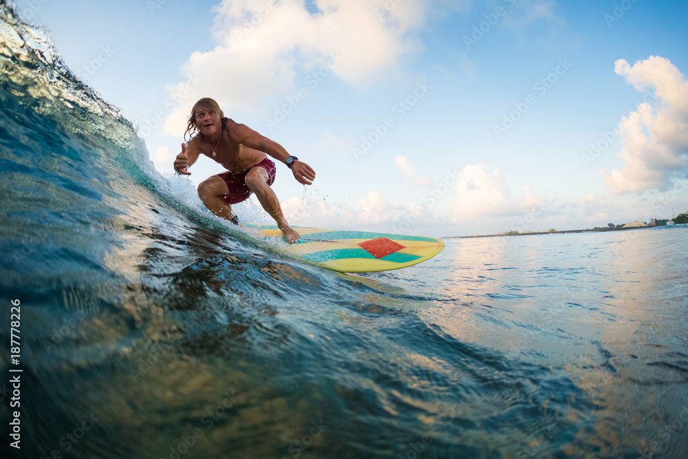 Young surfer rides ocean wave and shows the Shaka sign. Extreme sport and active lifestyle concept