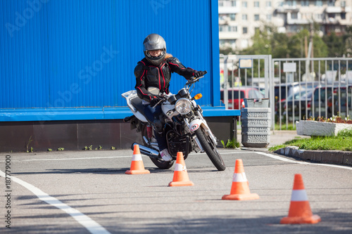L-driver person driving slalom through the orange cones on motordrome on motorcycle