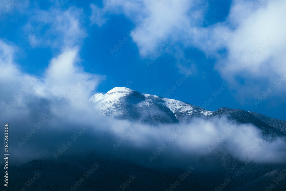 Beautiful foggy mountains high peaks covered with snow and ice. Morning winter alpine landscape, fog clouds, beautiful natural winter backdrop.