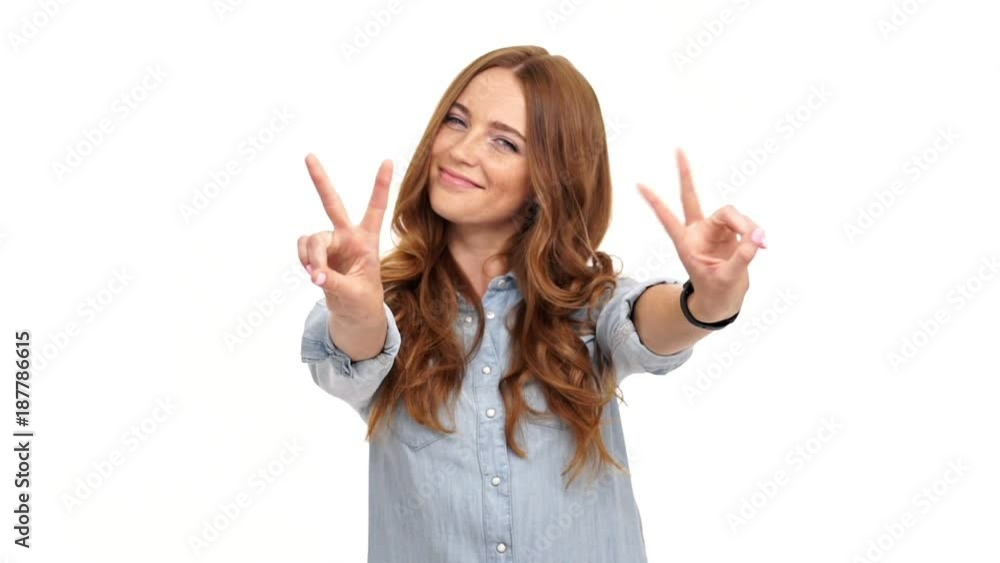 Happy ginger woman in denim shirt showing peace gestures and looking at camera over white background Happy ginger woman in denim shirt showing peace gestures and looking at camera over white background