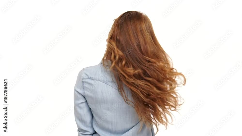Back view of young ginger woman in denim shirt playing with her hair and looking at camera over white background Back view of young ginger woman in denim shirt playing with her hair and looking at camera over white background