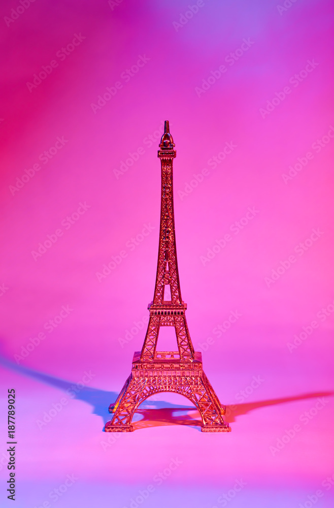 A golden statuette of the Eiffel Tower illuminated from both sides red and blue light