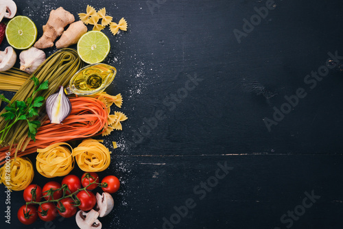 A set of pasta, noodles, spaghetti, tagliatelle, fettuccine, Farfalle. Italian cooking, fresh vegetables and spices. On a black wooden background. Top view. Copy space.