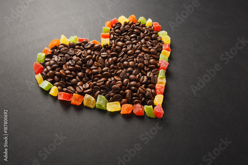 Colorful candied fruits in the form of heart with brown coffee beans isolated on black background for design. Saint Valentine's Day card on fabruary 14, holiday concept. Copy space for advertisement.