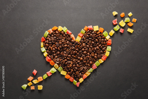 Candied fruits in the form of heart with arrow, brown coffee beans isolated on black background for design. Saint Valentine's Day card on fabruary 14, holiday concept. Copy space for advertisement.