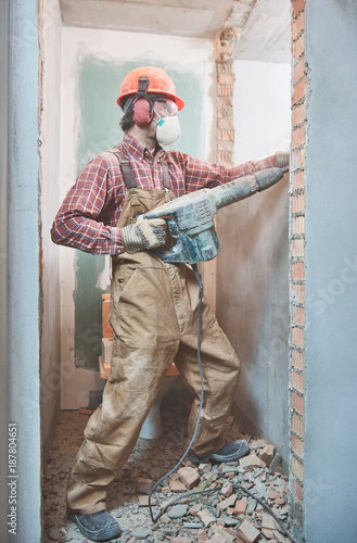 builder with demolition hammer breaking interior wall