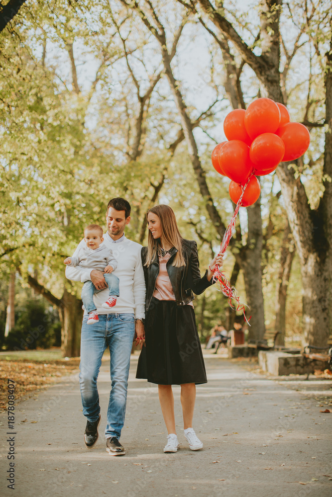 Happy young parents with baby boy in autumn park holding red balloons