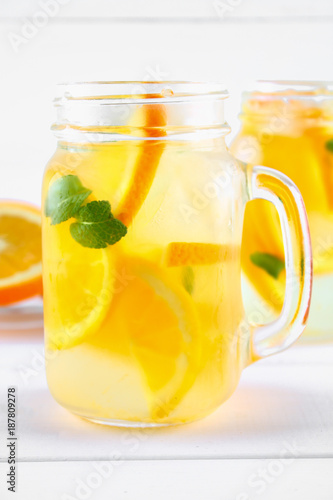 Orange detox water in mason jars on a white wooden table. Healthy food, drinks.