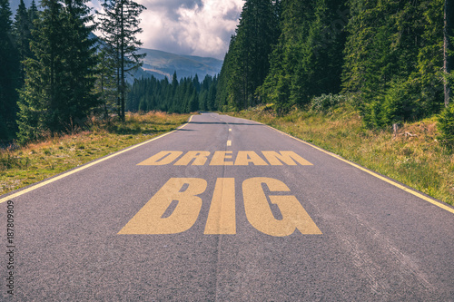 Asphalt road in the mountains going straight up with dream big text message. Conceptual business motivation background.
