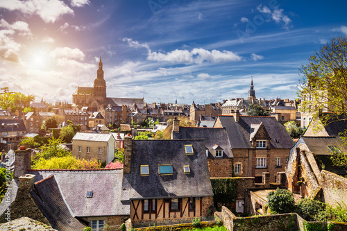 Fototapeta Naklejka Na Ścianę i Meble -  Beautiful view of scenic narrow alley with historic traditional houses and cobbled street in an old town of Dinan with blue sky and clouds. Brittany (Bretagne), France