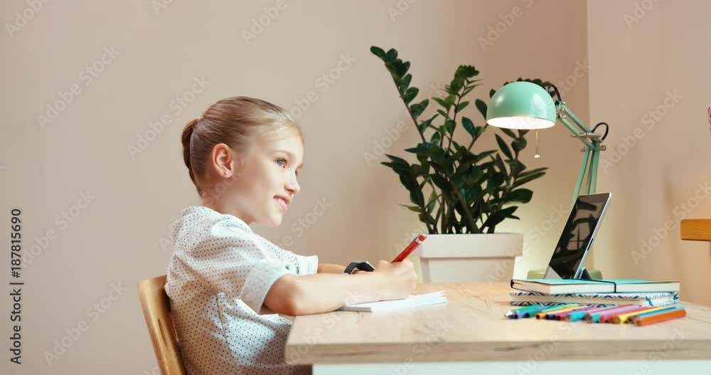 Cheerful school girl writing in notebook sitting at the desk Cheerful school girl writing in notebook sitting at the desk