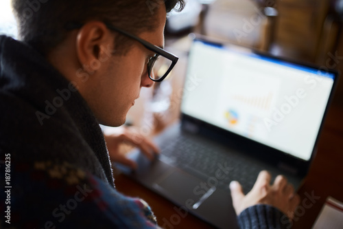 Close back view of businessman working with documents on laptop. Selective focus on stylish glasses. Freelancer browsing web in cafe. Poor eyesight threatment theme. photo