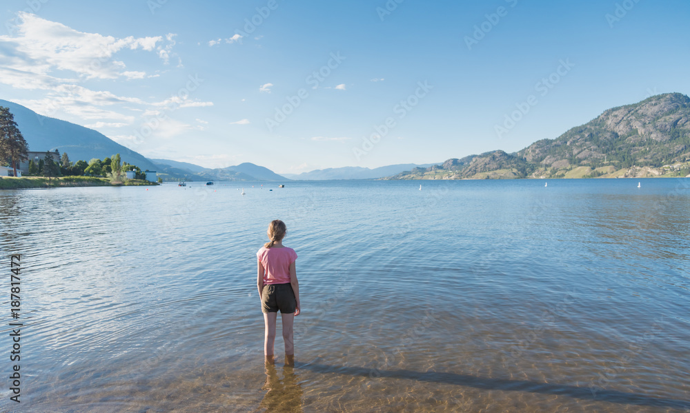 Young girl standing in Skaha Lake with back to camera looking north toward Penticton