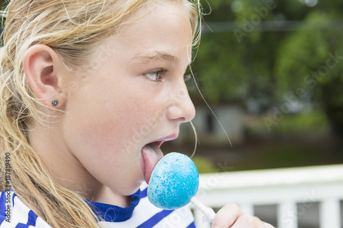 Tongue of Caucasian girl licking blue lollipop