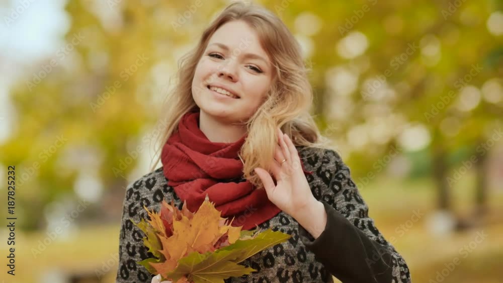 A young girl joyfully posing on the camera with a bouquet of colorful leaves. Walk in the city park in the autumn. A young girl joyfully posing on the camera with a bouquet of colorful leaves. Walk in the city park in the autumn.