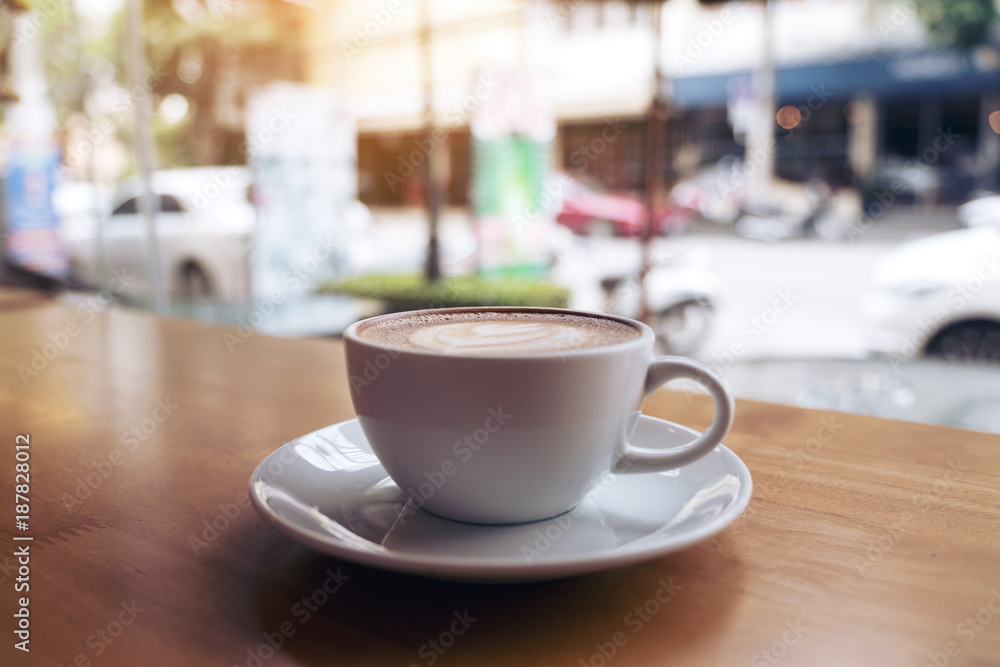 Closeup image of a white cup of latte coffee on wooden table in cafe with blur background Closeup image of a white cup of latte coffee on wooden table in cafe with blur background