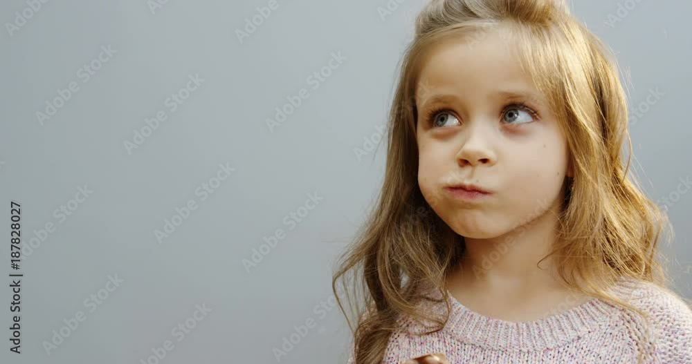 Close up of the blonde lovely funny little girl biting and eating a chocolate bar in front of the camera. White wall background. Portrait. Indoors Close up of the blonde lovely funny little girl biting and eating a chocolate bar in front of the camera. White wall background. Portrait. Indoors
