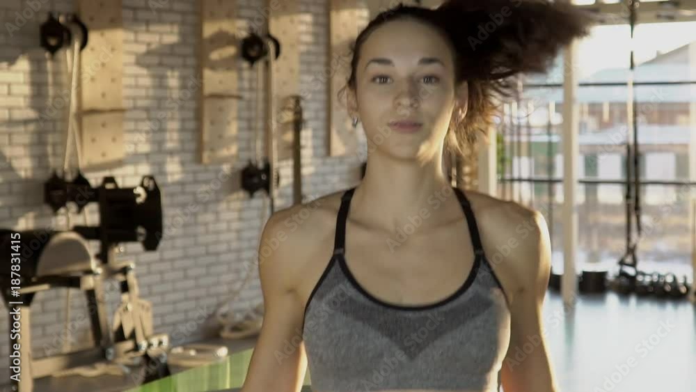 Portrait of a young female athlete jumping on a rope. In fitness club beautiful woman with long hair and dressed in a short top is engaged in cardio training on sports equipment. Portrait of a young female athlete jumping on a rope. In fitness club beautiful woman with long hair and dressed in a short top is engaged in cardio training on sports equipment.