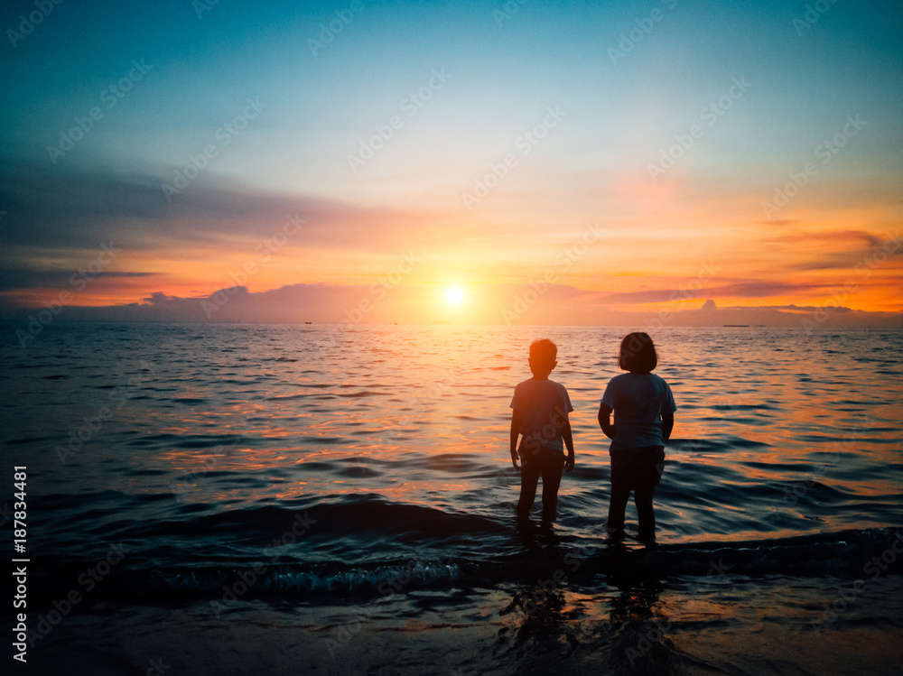 Little boy and girl stand together on the beach and looking at sea, while sunset, Holiday concept
