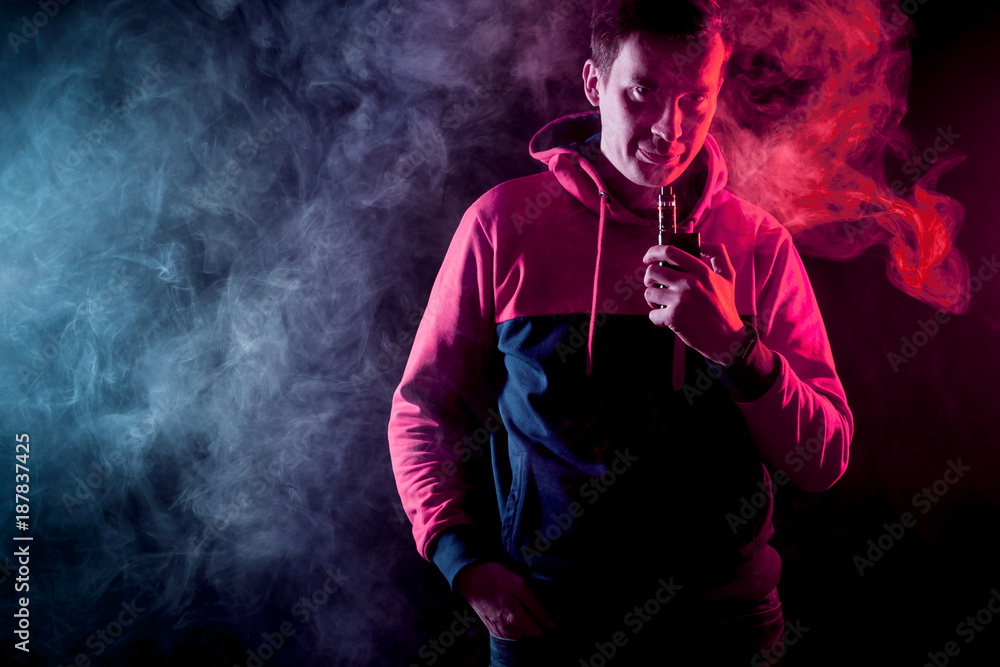 Man in sport hoody vaping an electronic cigarette.Isolated on black background.Around  clouds of smoke