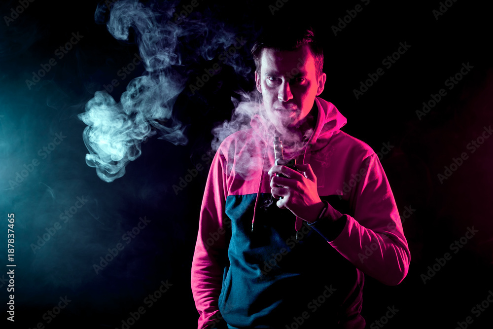 The man smoke an electronic cigarette on a background of red and blue smoke The man smoke an electronic cigarette on a background of red and blue smoke