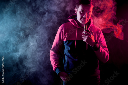 Man in sport hoody vaping an electronic cigarette.Isolated on black background.Around clouds of smoke