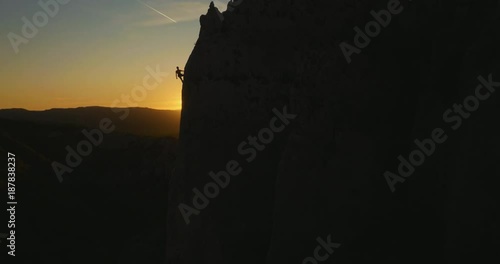Aerial wide shot of a rock climber descending the wall  at amazing evening sunset light.
