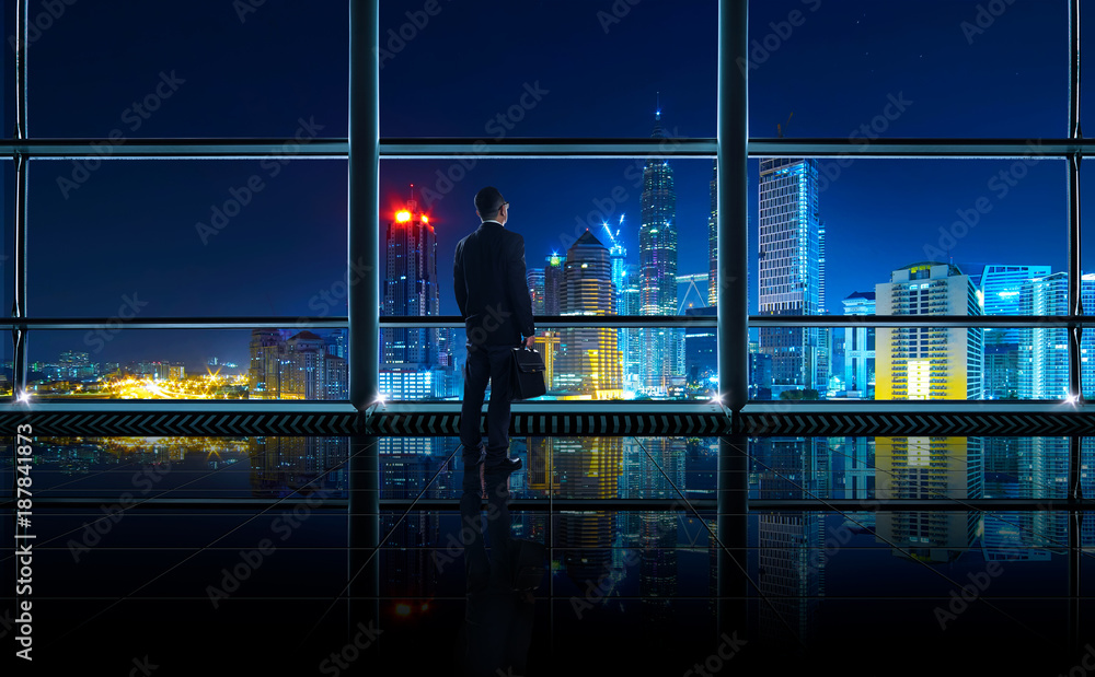 Back view of thoughtful businessman looking out of big office window at office ,planning future project concept, night scene . Back view of thoughtful businessman looking out of big office window at office ,planning future project concept, night scene .