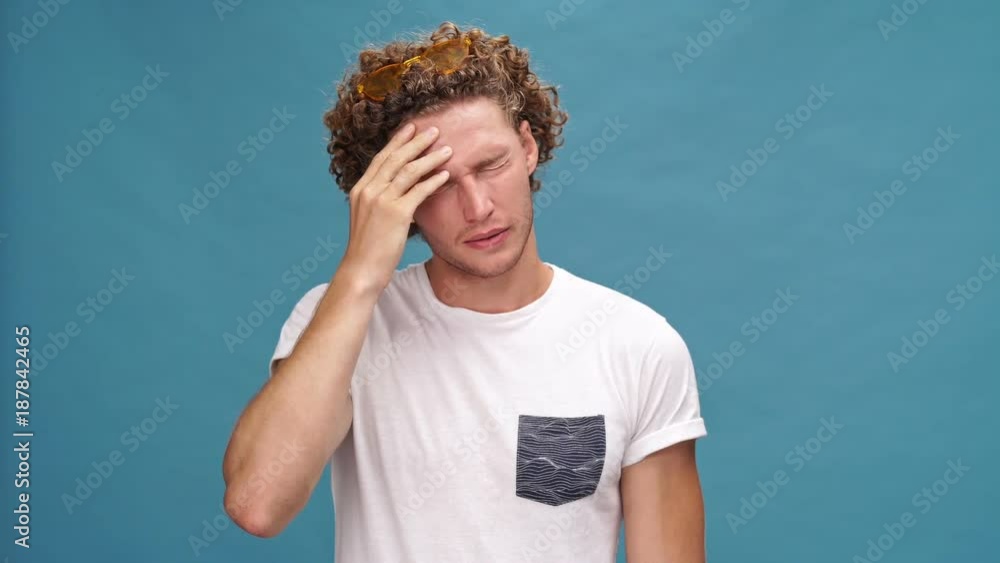 Confused curly man in t-shirt forgot something to do over blue background Confused curly man in t-shirt forgot something to do over blue background