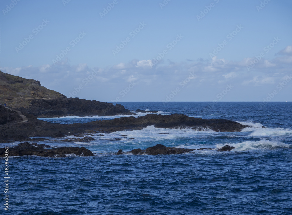 natural background - lava rock sea shore with blue sea and waves foam blue sky background natural background - lava rock sea shore with blue sea and waves foam blue sky background