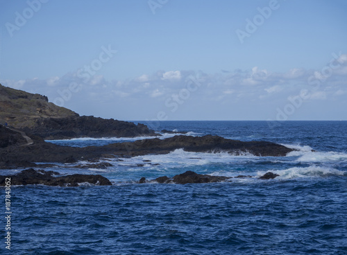natural background - lava rock sea shore with blue sea and waves foam blue sky background